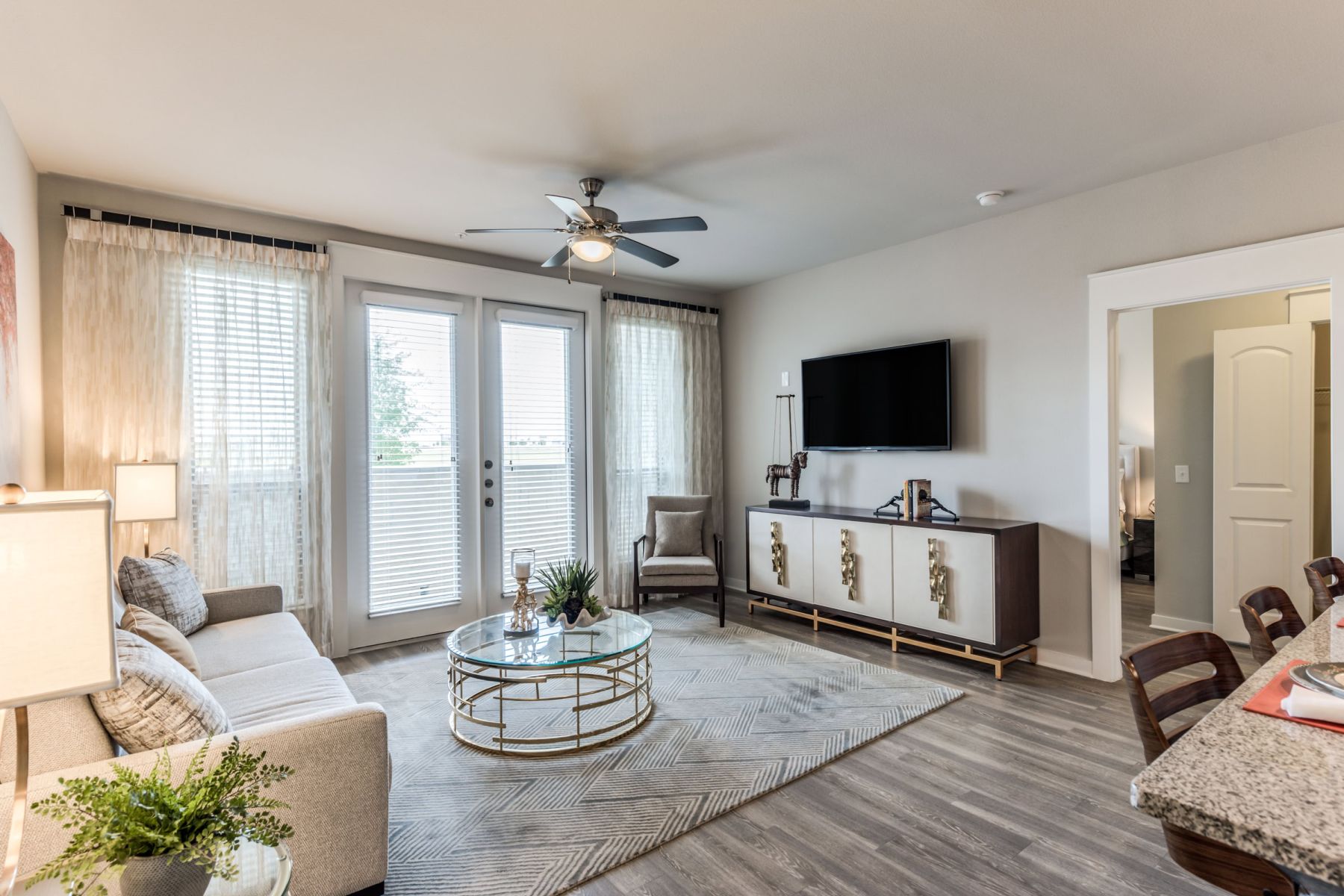 Empty room with wood floors, ceiling fan, and sliding glass door leading to a patio with vertical blinds at Apex West Midown.